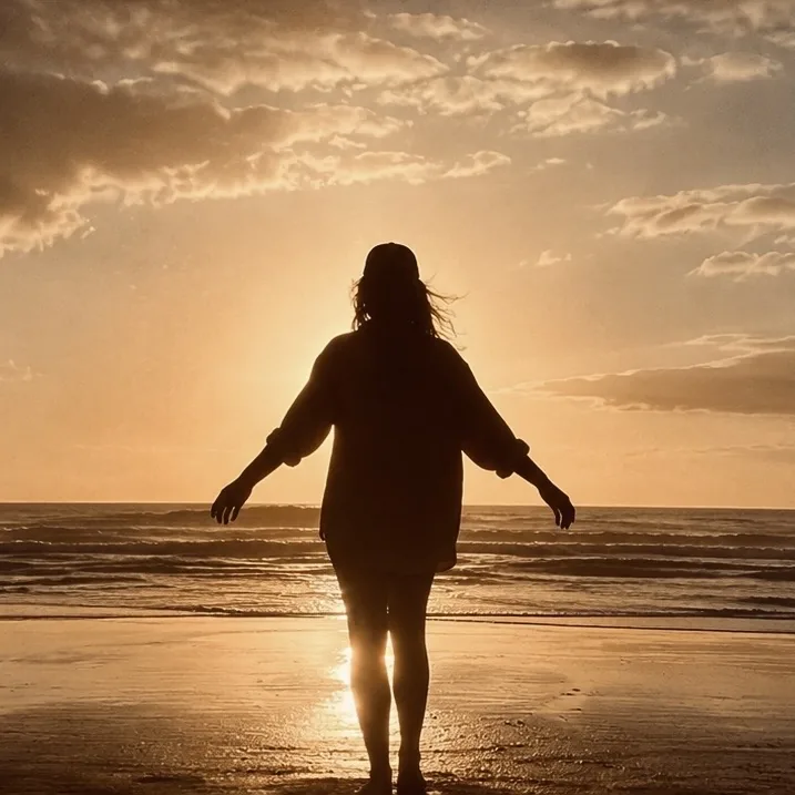 Silhouette einer Frau mit ausgebreiteten Armen am Strand bei Sonnenuntergang